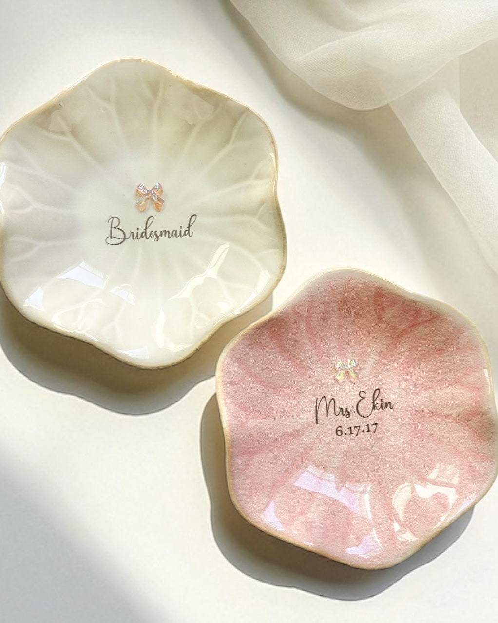 Two ceramic trinket dishes, one white and one pink, with personalized text on a light background.